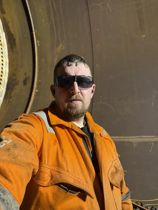 Dru in orange welding suit wearing protective eye wear and earplugs